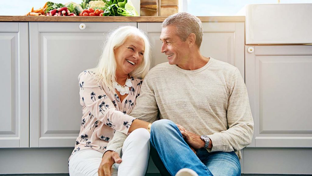 A senior couple laughing in a kitchen, discussing infrared saunas